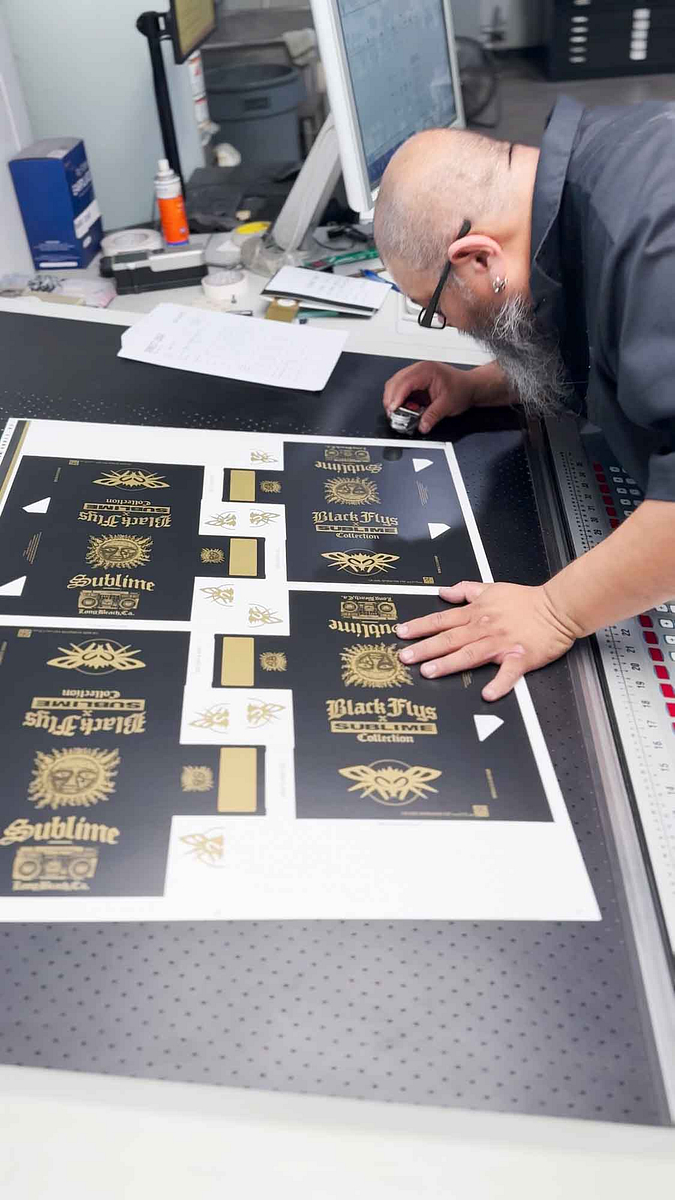 Image showing an employee checking color accuracy of a production run of Black Fly sunglass boxes coming off the Koenig and Bauer Press.