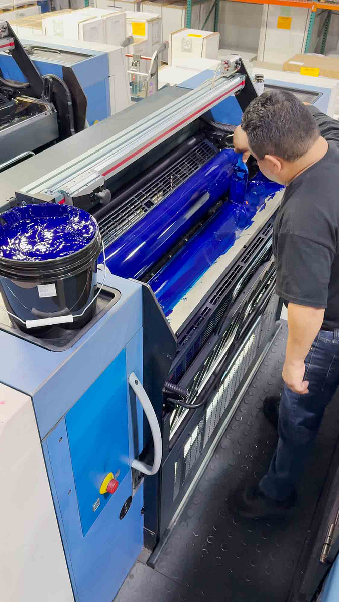 Image of an employee applying ink to the rollers of a Koenig and Bauer press.